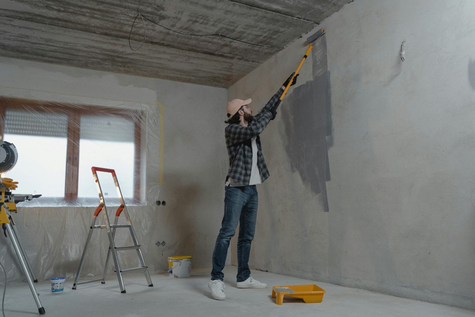 A man painting an interior wall with a roller during a home renovation project.